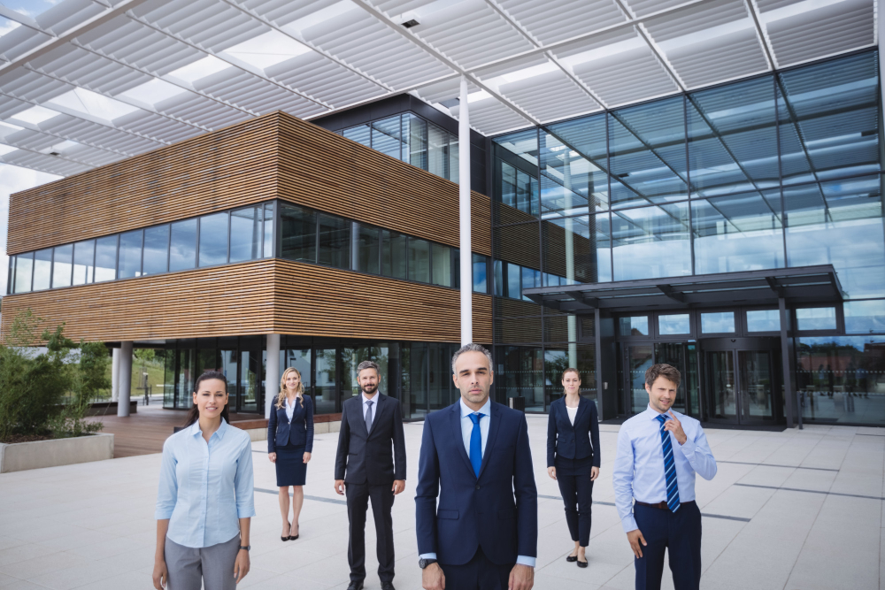 A team of corporate legal and compliance professionals standing confidently outside a modern glass-and-wood commercial office building in Singapore, representing business expansion strategies.
