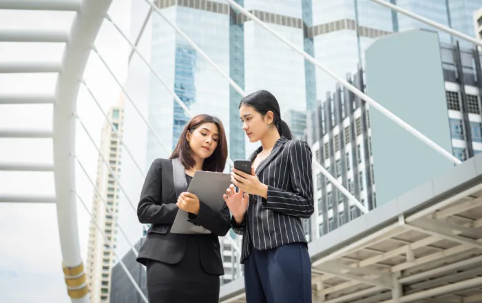 Two female corporate advisors in a modern financial district reviewing Singapore holding company setup details on a smartphone.