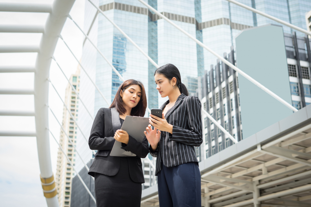 Two female corporate advisors in a modern financial district reviewing Singapore holding company setup details on a smartphone.