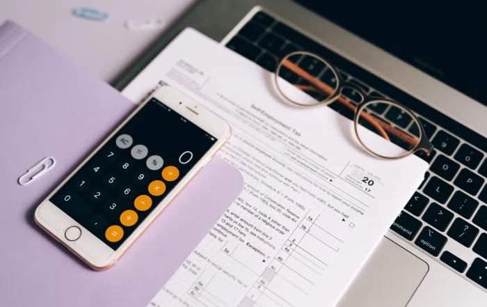 A smartphone with a calculator app on tax documents next to a laptop, emphasizing modern accounting.