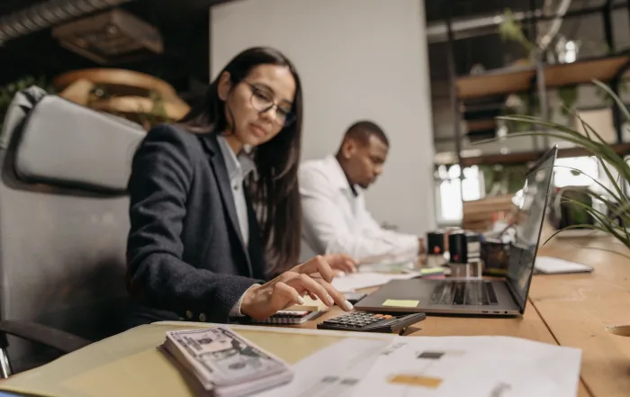 Two business professionals collaborating with a laptop and calculator in a modern office