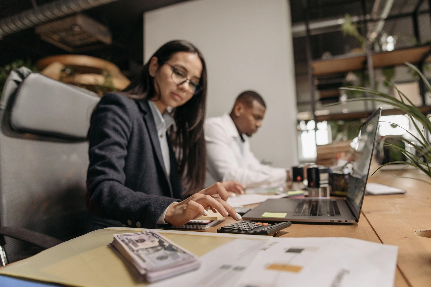 Two business professionals collaborating with a laptop and calculator in a modern office